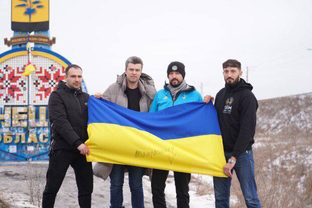 Чоловіки з українським прапором на фоні стели Донецької області