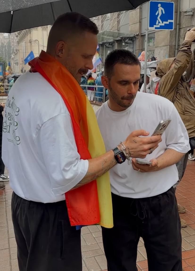 Чоловік у білому одязі з прапором ЛГБТК+ на шиї