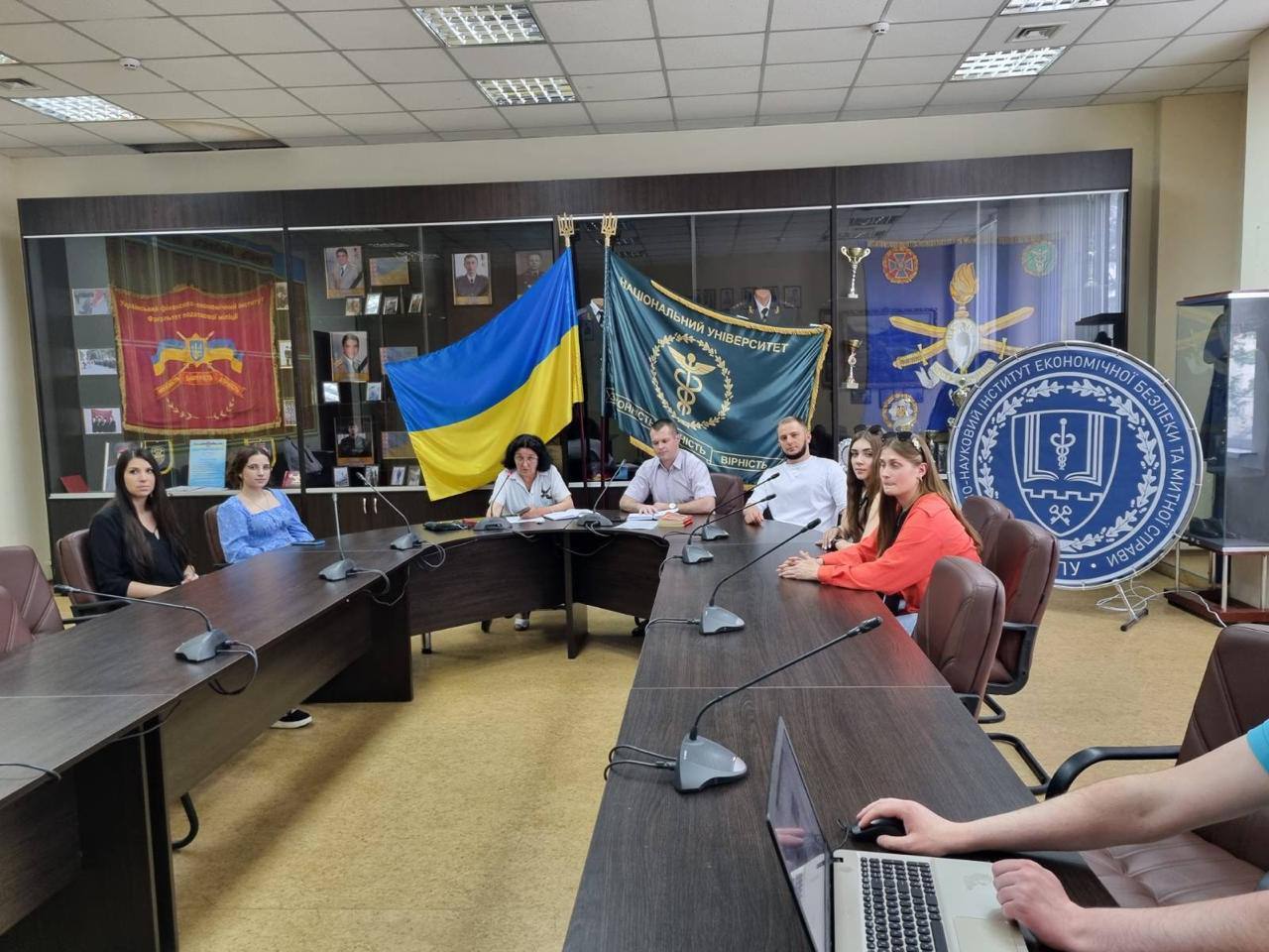 Люди сидять за столом на фоні прапору України