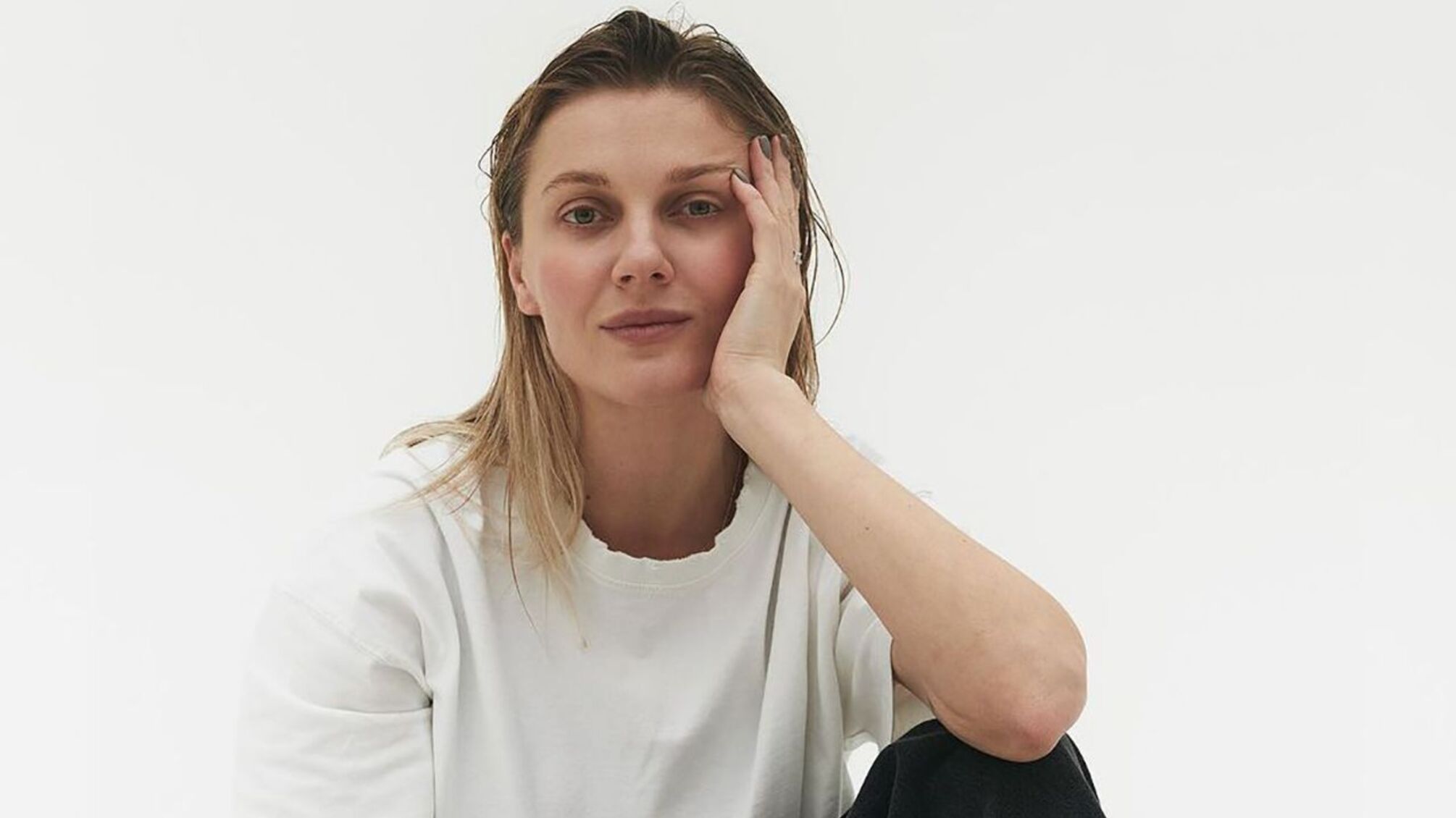 Украинская певица Kola в белой футболке и черных брюках на белом фоне.