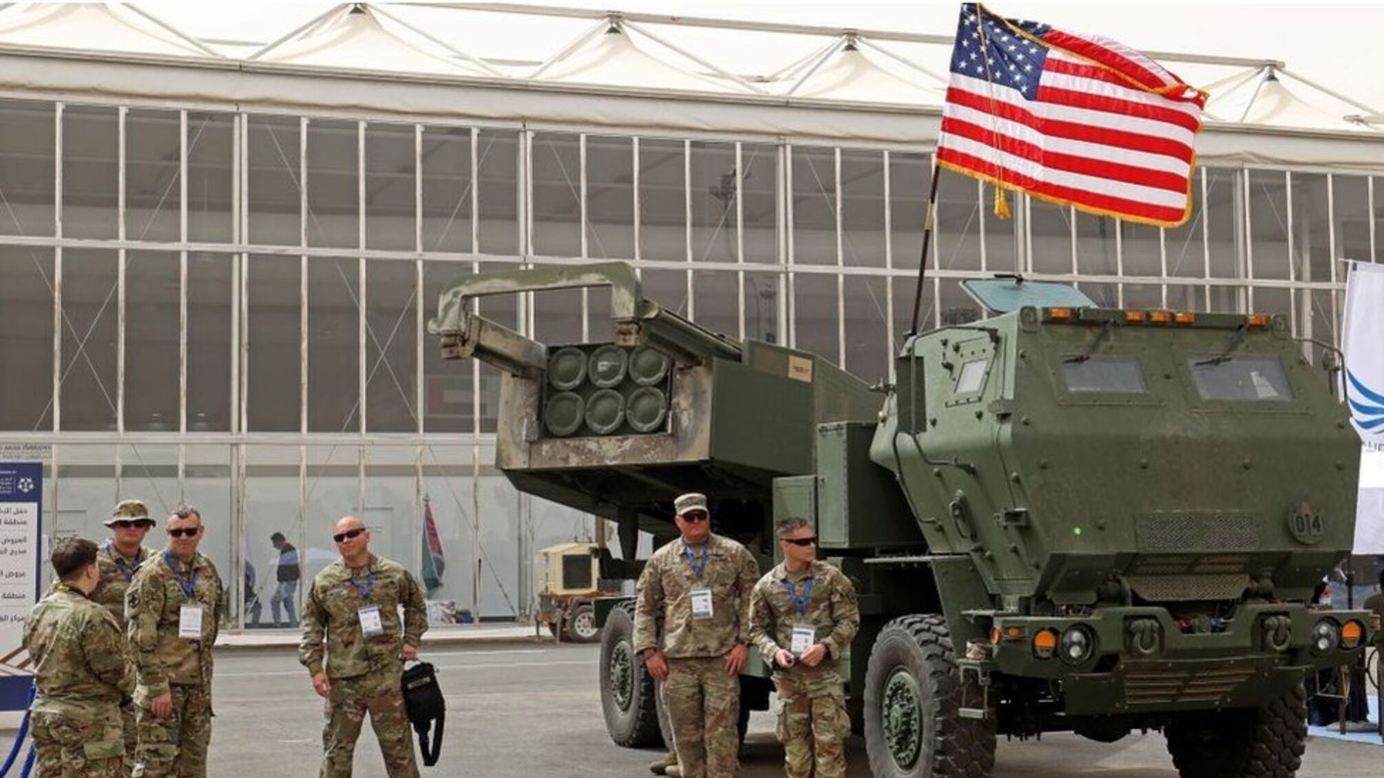 Чоловіки у військовій формі на фоні техніки та прапору США