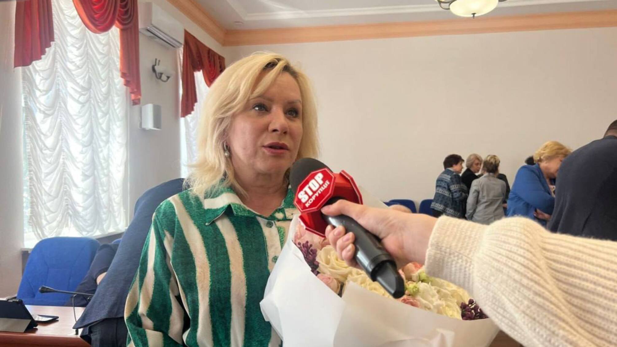 Женщина в рубашке с цветами и микрофоном.