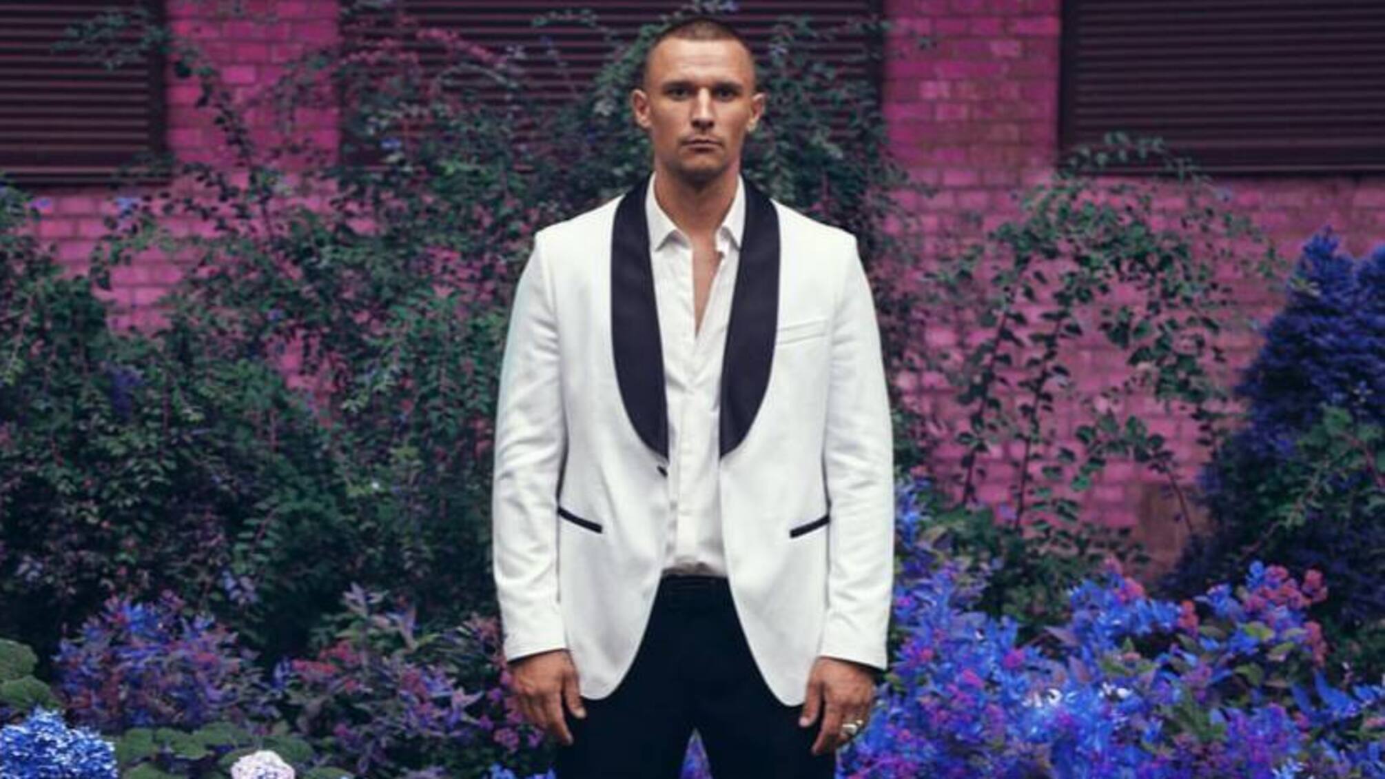 Тарас Цымбалюк в белом костюме на фоне цветов.